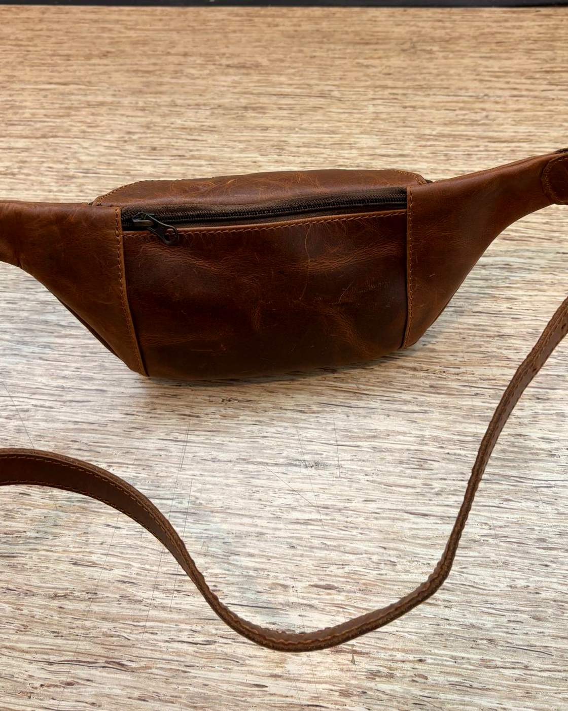 Real photo of the back of the Nomad Sling, showing a single zipped pocket set into the back panel and the strap trailing away across the table.