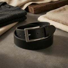 The Draftsman black leather belt coiled, showing the edge stitching and gunmetal buckle. — view 4