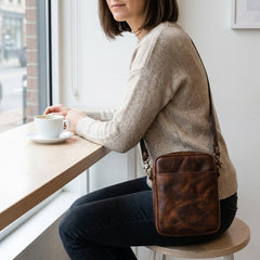 A woman seated at a cafe wearing the Bellvari YYZ Travel Satchel crossbody. — view 8