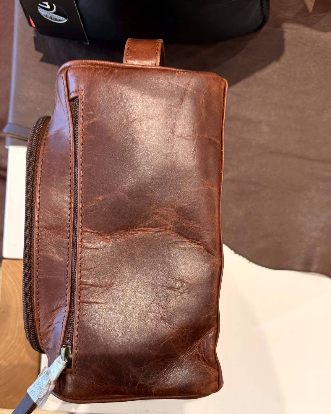 Real photo of the dopp kit from the side, showing the leather carry loop at the top end and the zip running down the side.